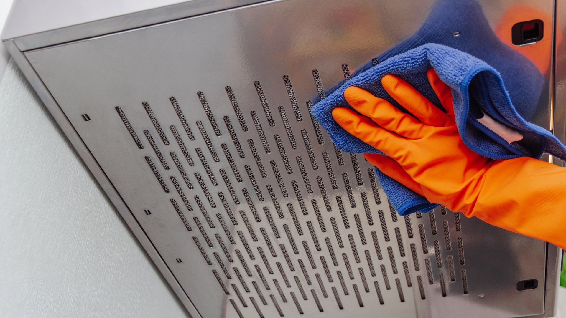 Orange gloved hand cleaning metal surface with blue microfiber cloth
