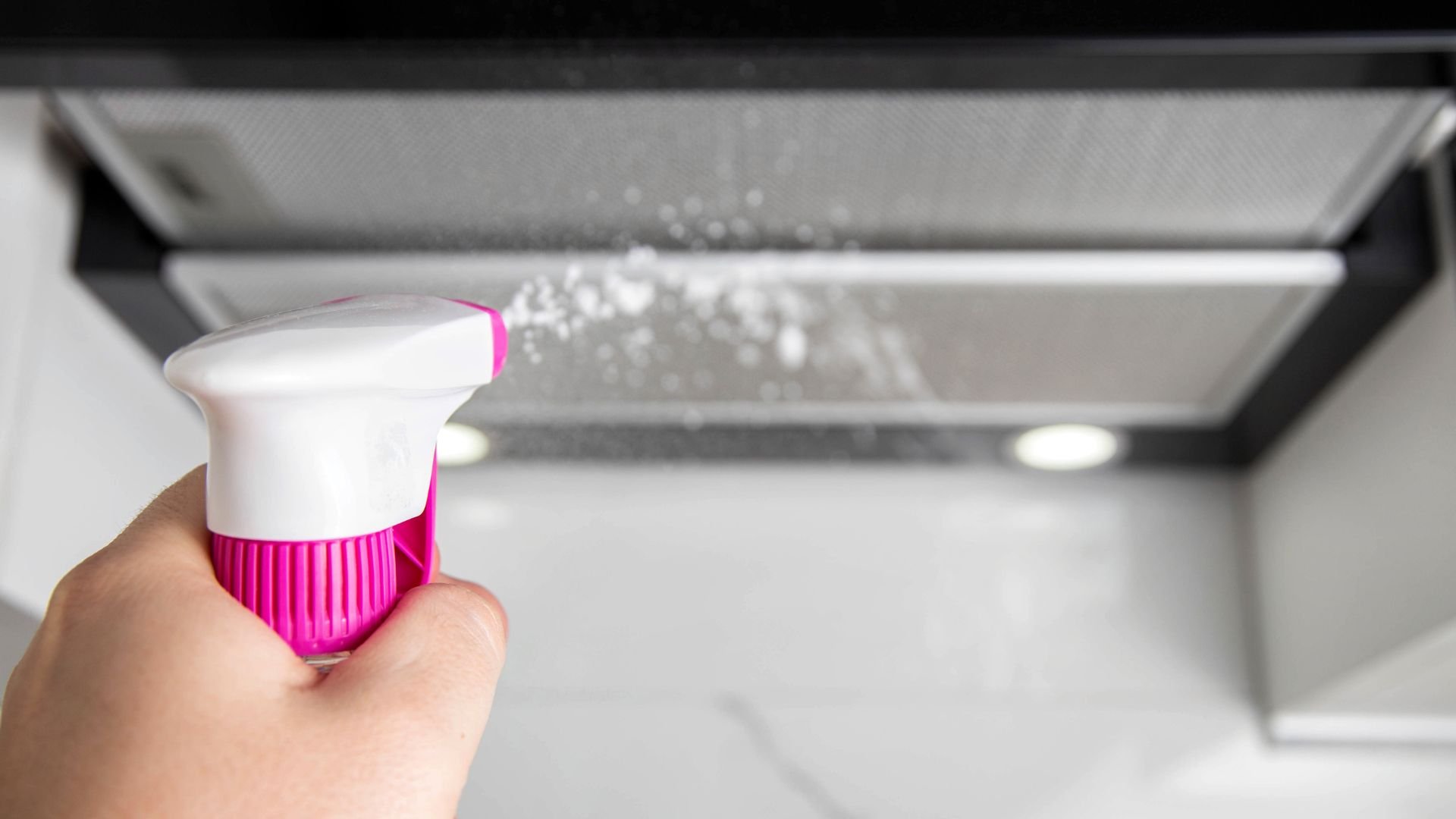 Hand holding pink and white cleaning brush near kitchen range hood